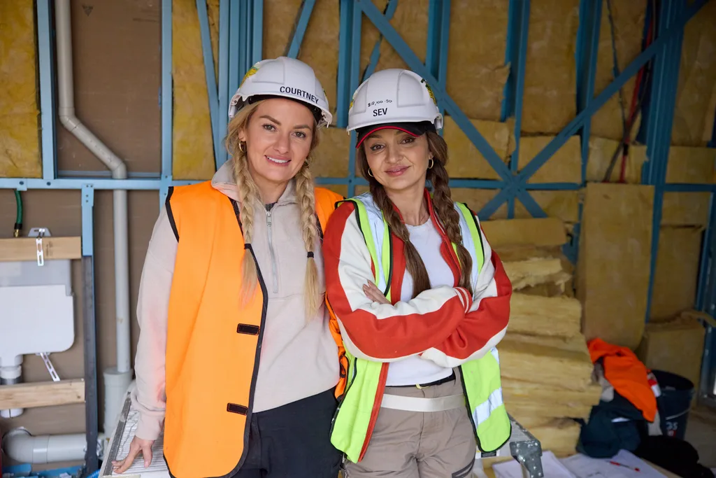 courtney and sev, two women standing posing for the camera with smiles, dressed in construction gear