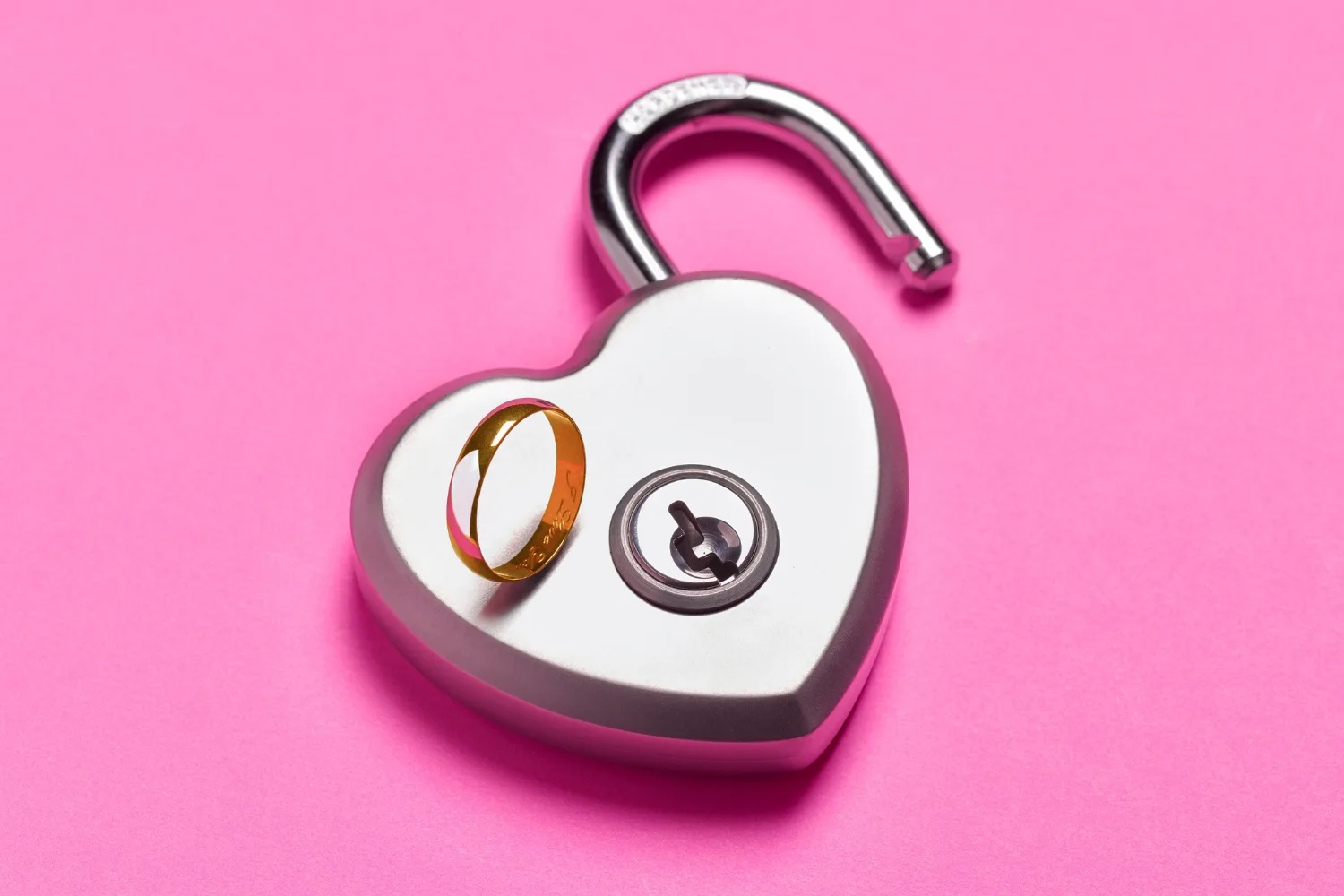 Wedding ring sitting on open padlock - stock photo.