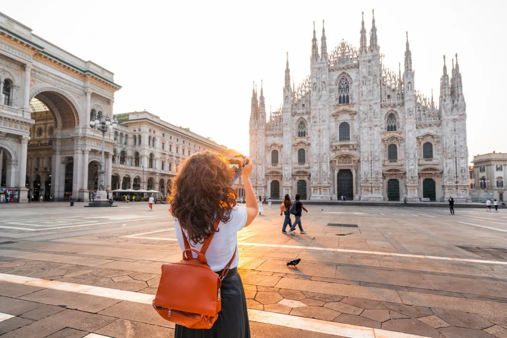 A female traveler with a backpack taking a photograph of the Milan Cathedral (Duomo di Milano) in Italy.