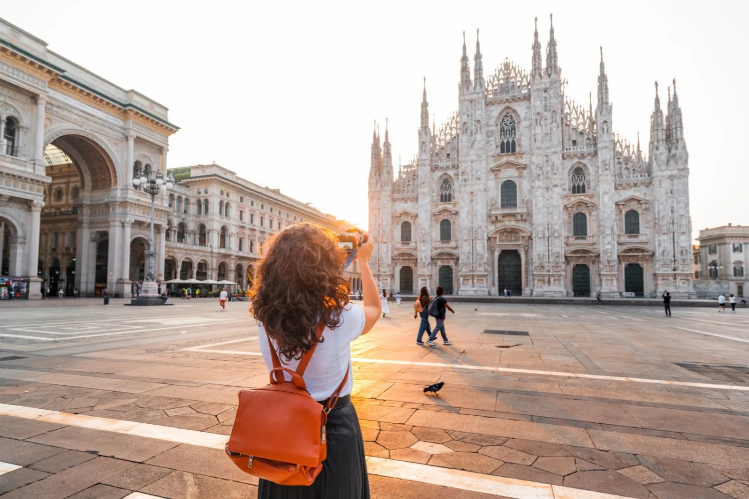 A female traveler with a backpack taking a photograph of the Milan Cathedral (Duomo di Milano) in Italy.