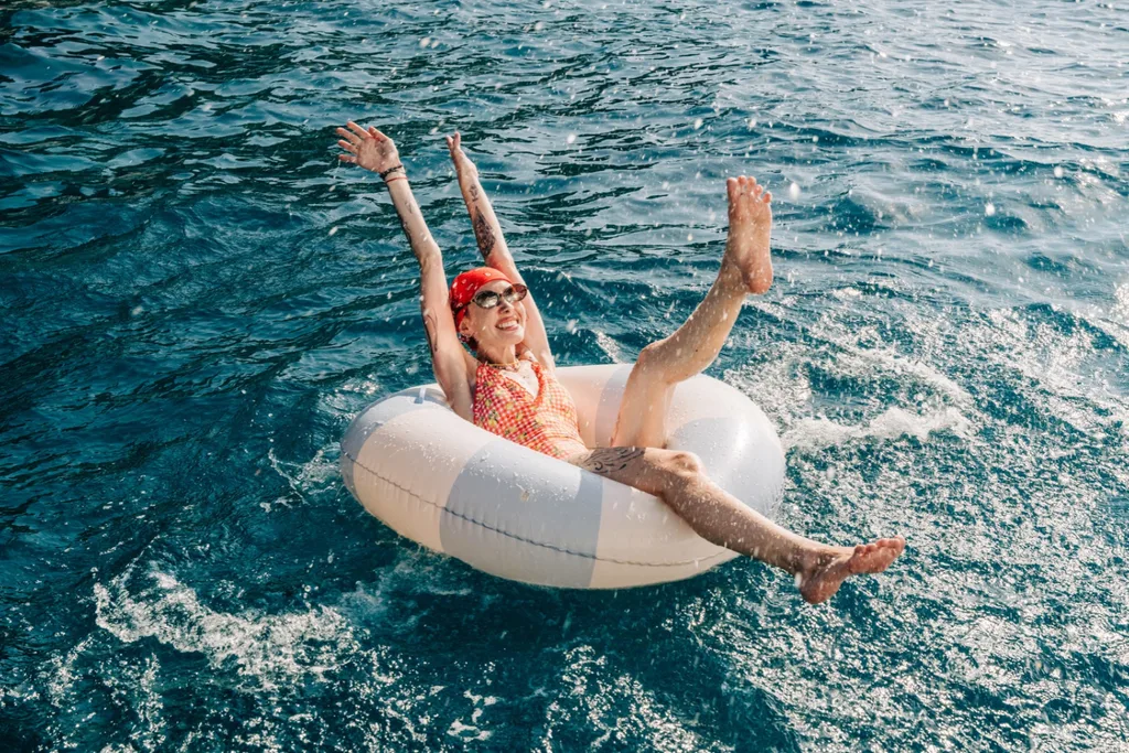 A happy person in a red bandana and sunglasses splashing water while floating on an inflatable ring in the ocean.