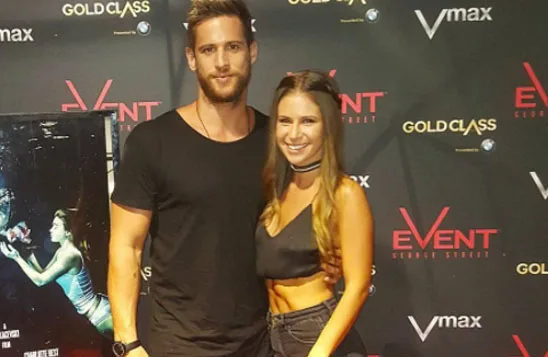 Young man and woman posing in front of an Event Cinemas backdrop at a premiere, man in black shirt, woman in crop top.