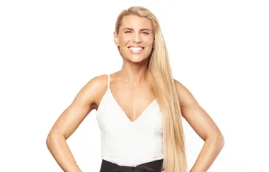 A woman with long blonde hair smiles confidently, wearing a white top.