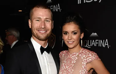 Man in a tuxedo and woman in a lace dress smiling at a formal event.