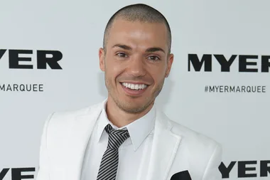 Man in a white suit and black tie smiling at a Myer event backdrop.