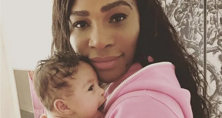 A woman in a pink hoodie holds a baby close, both looking at the camera.