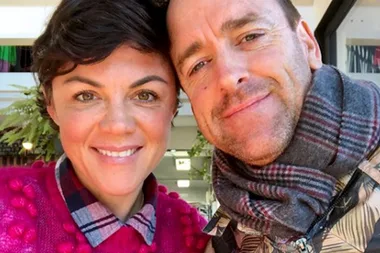A smiling couple takes a close-up selfie indoors, both wearing cozy clothing.