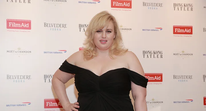 A woman in a black dress at a FilmAid event backdrop with Belvedere Vodka and Hong Kong Tatler logos.