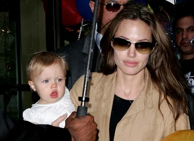 {"alt":"Woman with sunglasses holding a toddler in a white outfit."}