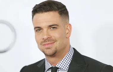 A man with short dark hair in a suit and checkered shirt, smiling at a formal event.