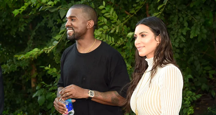 Two people standing outdoors, smiling, with leafy green background.