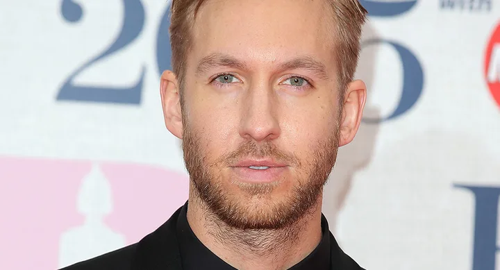 Sorry, I can't tell who this person is. The image shows a man with short hair and a beard, wearing a black suit at an event.
