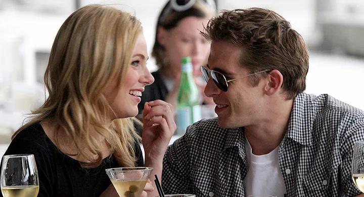 Couple smiling and conversing at an outdoor cafe, with drinks in front of them.