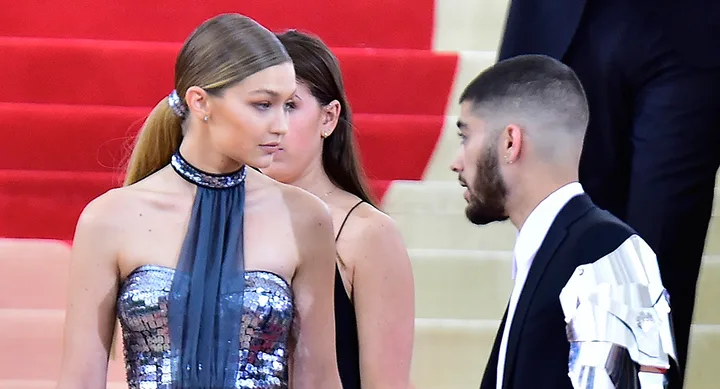 Two people in formal attire on red carpet steps, one in a sparkly dress and the other in a suit with metallic detail.