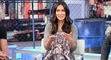 Actress in a patterned dress speaks on a panel with industrial backdrop.