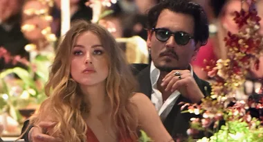 ```plaintext
A man in sunglasses sits with a woman, surrounded by flowers at an event.
```