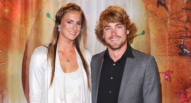 A man and woman smiling at an event with a colorful backdrop.