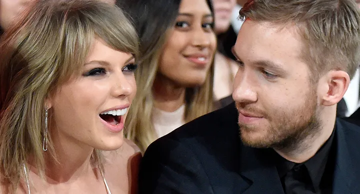 Two people sitting closely, smiling and talking at an event, with blurred audience in the background.