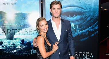 A couple poses in front of "In the Heart of the Sea" movie poster at a premiere event.