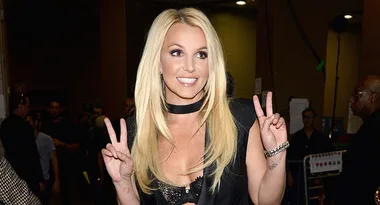 Blonde woman smiling and making a peace sign with both hands indoors.
