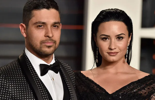Two people posing together, with one wearing a polka dot suit and the other a black dress, at a formal event.