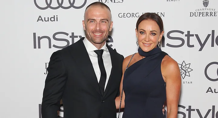 A man and woman in formal attire smiling on the red carpet at an InStyle event.