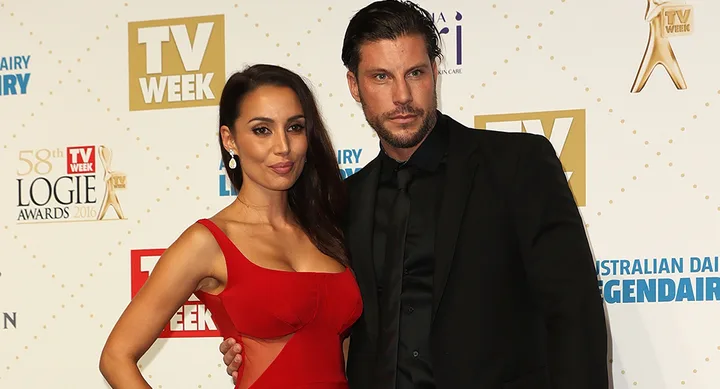 Two people posing on the red carpet at the 2016 Logie Awards. The woman is wearing a red dress and the man a black suit.