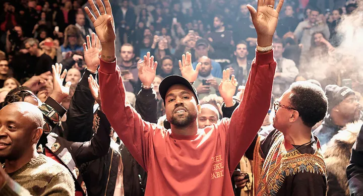 Man in a red sweatshirt raises hands at a crowded event, surrounded by people doing the same.