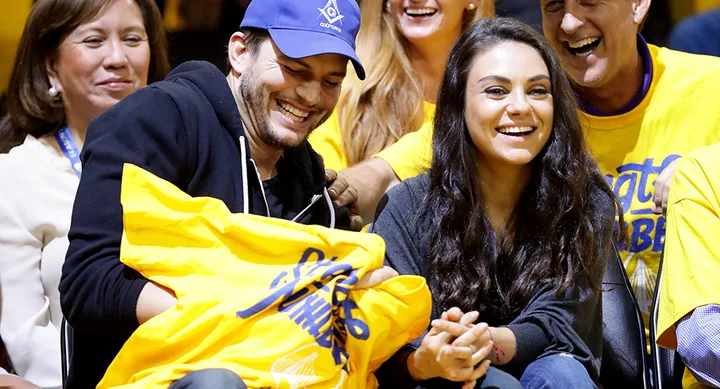 Two people smiling and laughing at a sporting event, surrounded by others in yellow shirts.