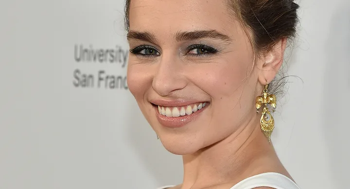 Smiling woman with updo hairstyle, gold earrings, and white top.