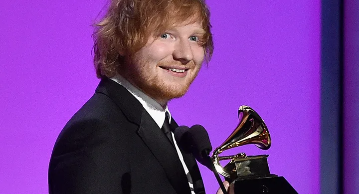 Person in a suit smiling while holding a Grammy award against a purple background.
