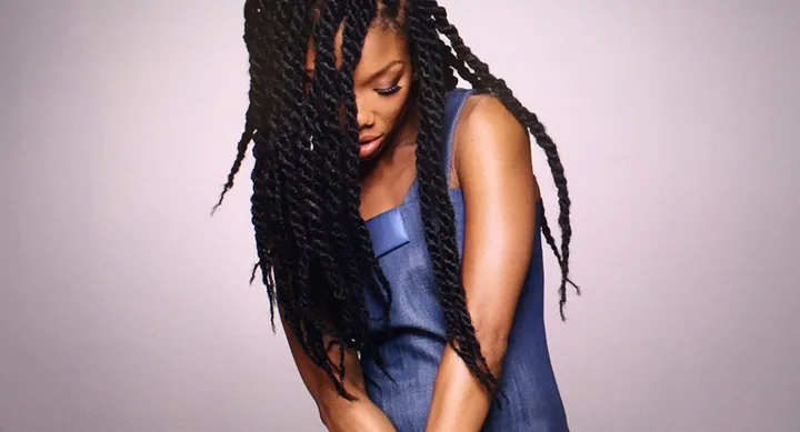 A person with long braided hair wearing a blue sleeveless top, looking down.