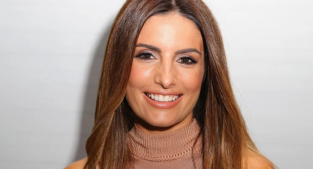 A woman with long brown hair smiling, wearing a brown turtleneck against a plain background.