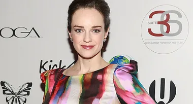 A person in a colorful dress smiles at a formal event with logos in the background.