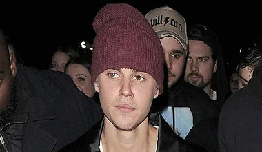 A person wearing a maroon beanie surrounded by a crowd at night with a focused expression.