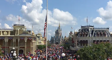 Crowded Main Street at Disney World with Cinderella Castle in background, flags waving, and clear blue skies.