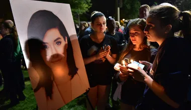 Group of people holding candles in front of a large photo at a nighttime vigil.