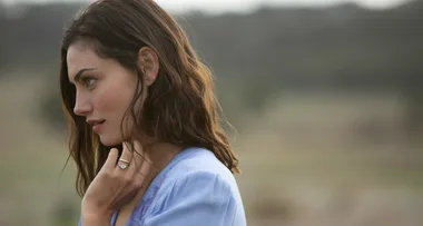 A woman with brown hair in a lavender blouse gazes to her left in a serene outdoor setting.