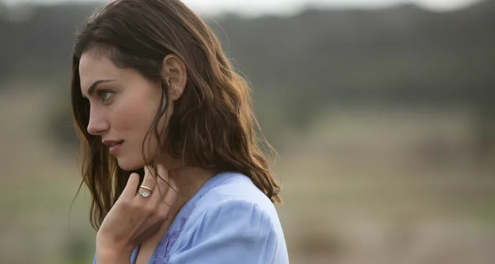 A woman with brown hair in a lavender blouse gazes to her left in a serene outdoor setting.