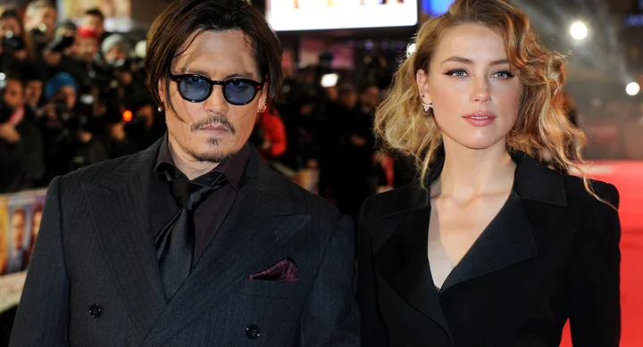 A man in sunglasses and a woman with curly hair pose together on a red carpet event.