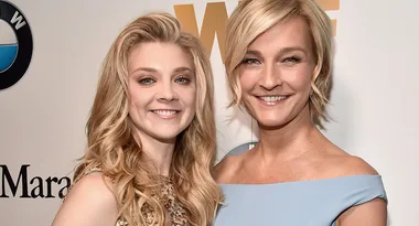 Two women smiling at a red carpet event, posing together against a branded background.