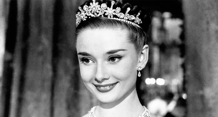 A woman with a floral tiara, smiling elegantly, in a black-and-white photo.