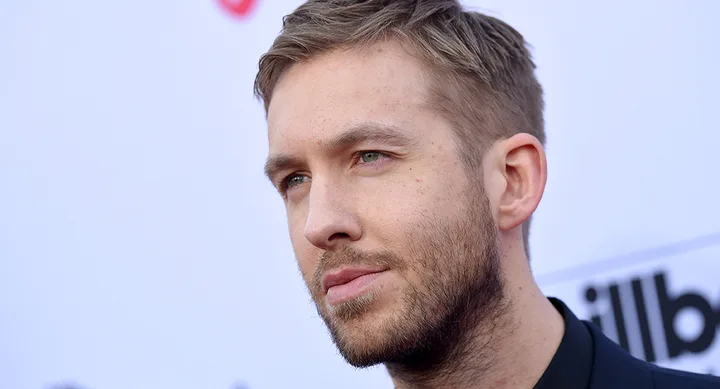 A person with short hair and a beard looking to the side at a Billboard event backdrop.