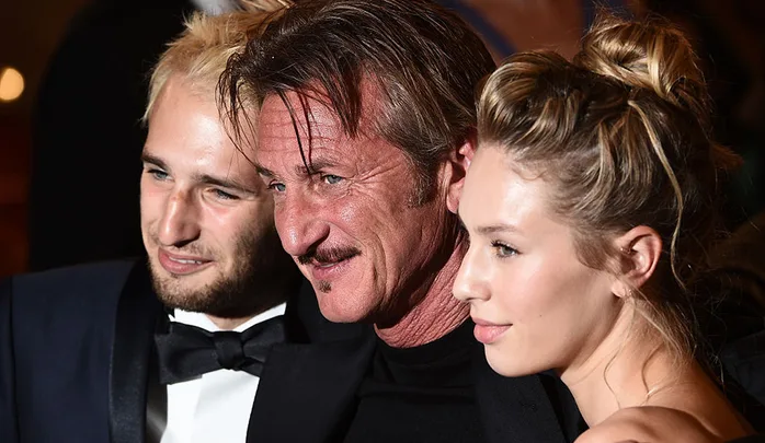 Three people posing closely at a formal event, with one man in the center smiling broadly.