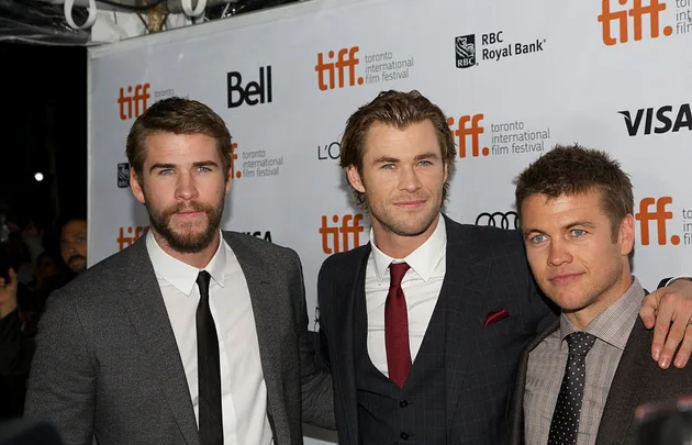 Group of three men in suits at the Toronto International Film Festival, posing for a photo on the red carpet.