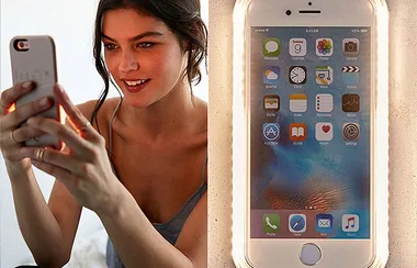 Young woman taking a selfie with a smartphone; phone screen displays various app icons.