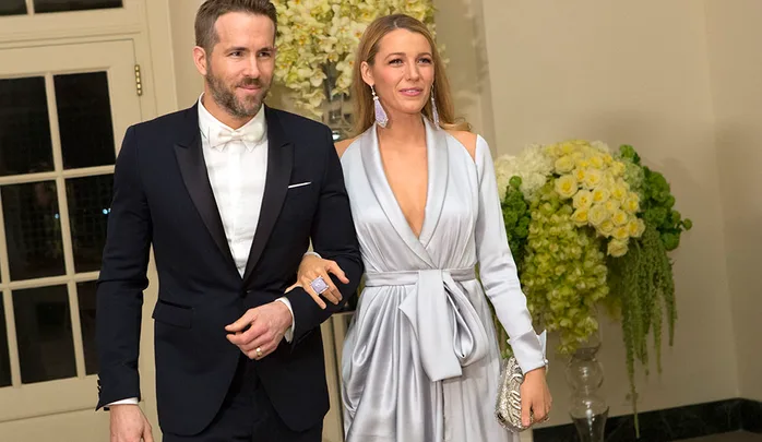 Couple dressed formally, man in a black suit with bowtie, woman in a silver gown, posing arm in arm indoors.