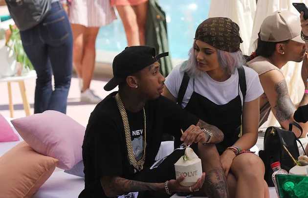 People sitting by a poolside, one holding a coconut drink, chatting and relaxed at an outdoor event.