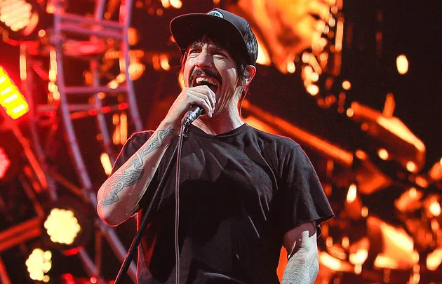 Lead singer wearing a black shirt and cap, performing passionately on stage with bright lights in the background.