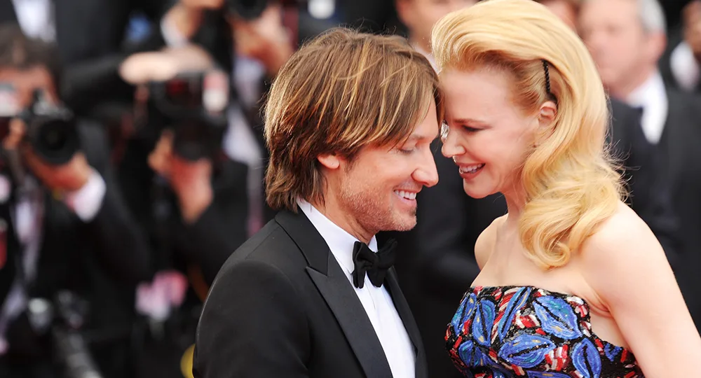 Two people smiling and standing close on a red carpet, surrounded by photographers.